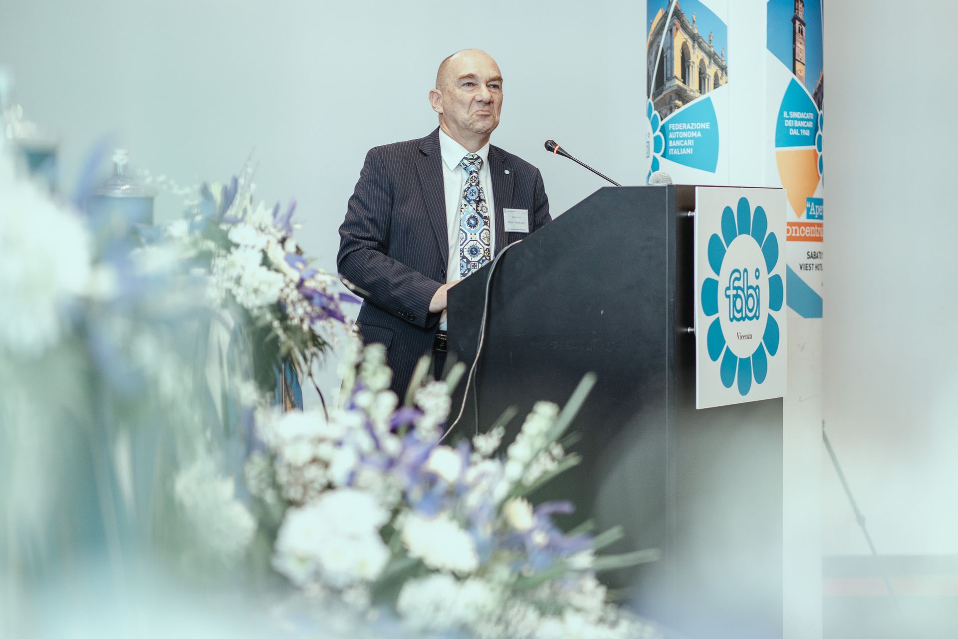 Un uomo in giacca e cravatta è in piedi su un podio e tiene un discorso.