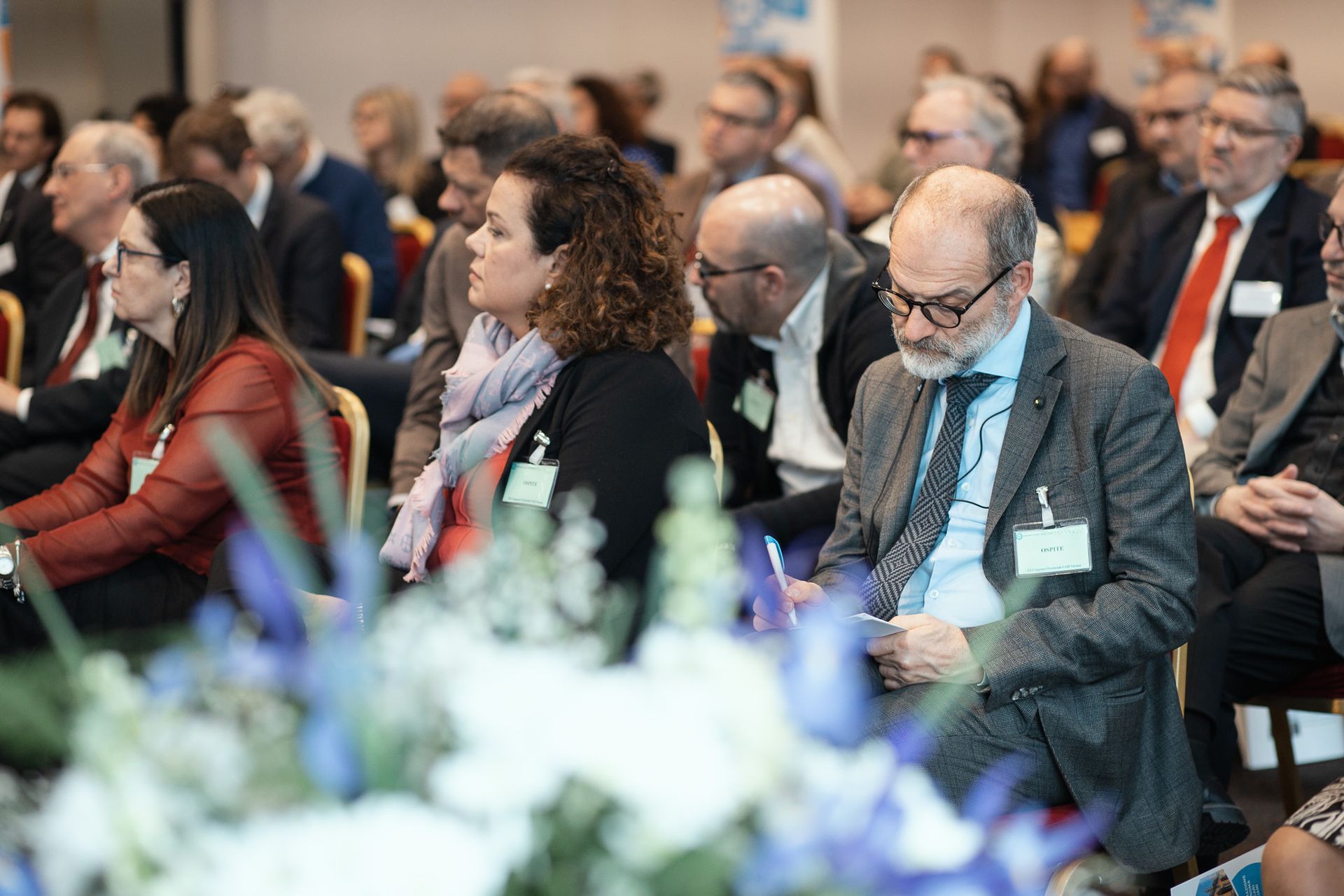 Un gruppo di persone è seduto in una stanza con fiori in primo piano.