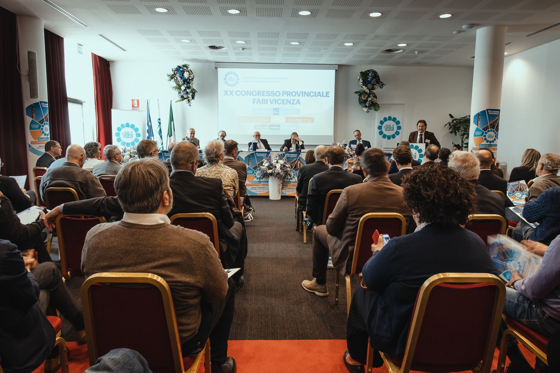 Un folto gruppo di persone è seduto in una sala conferenze e guarda una presentazione.