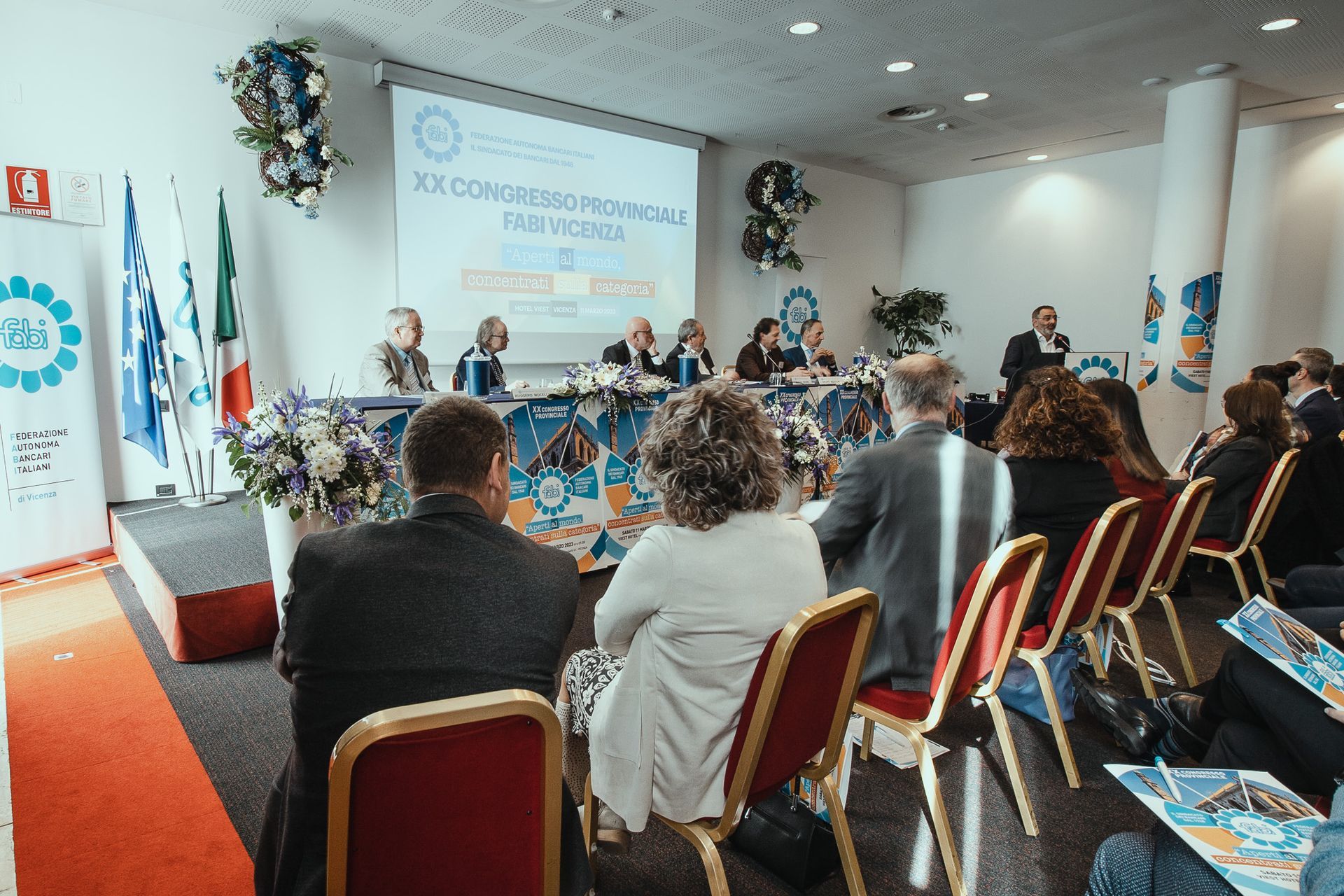 Un gruppo di persone è seduto su delle sedie davanti a un grande schermo.