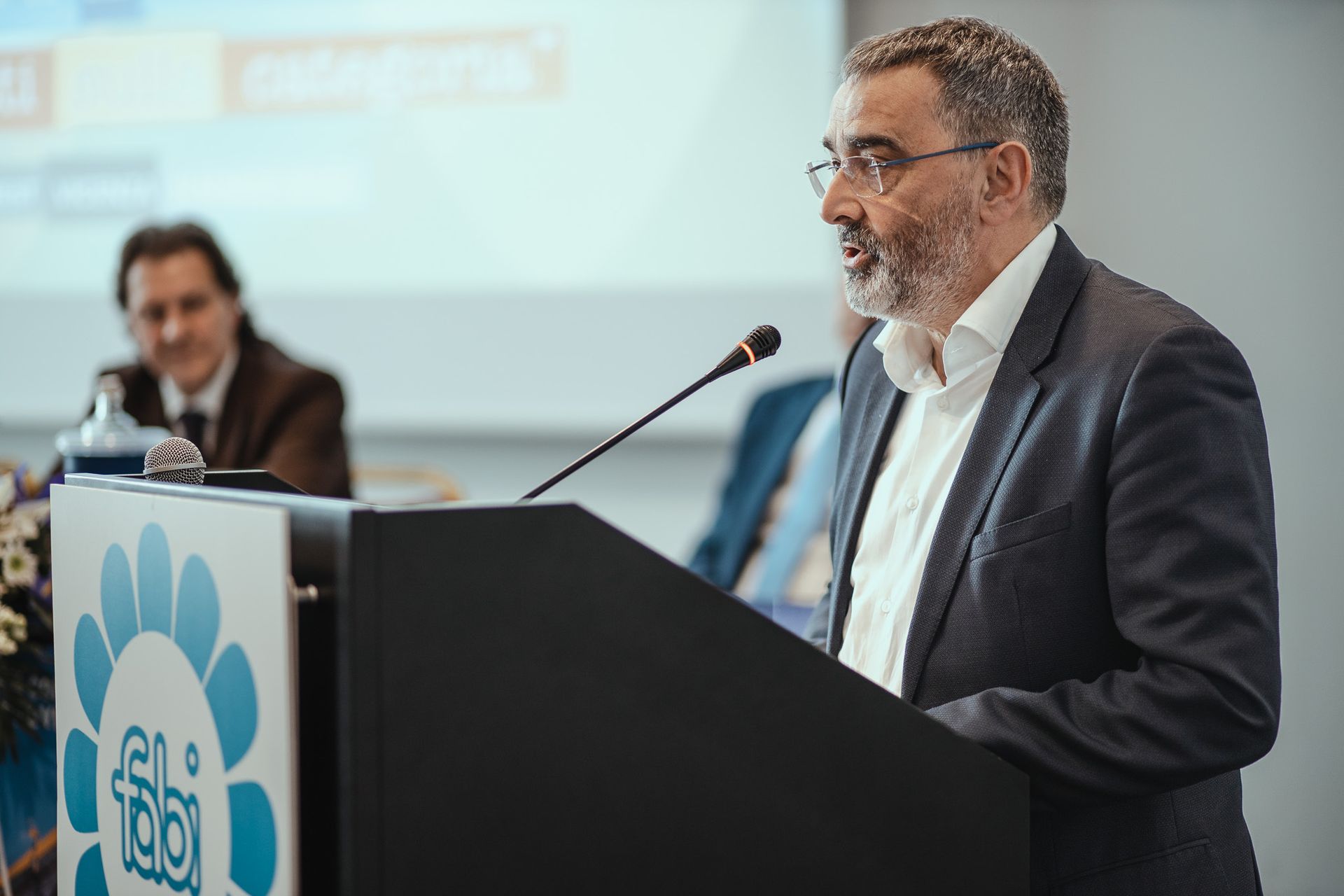 Un uomo in giacca e cravatta è in piedi su un podio e parla al microfono.