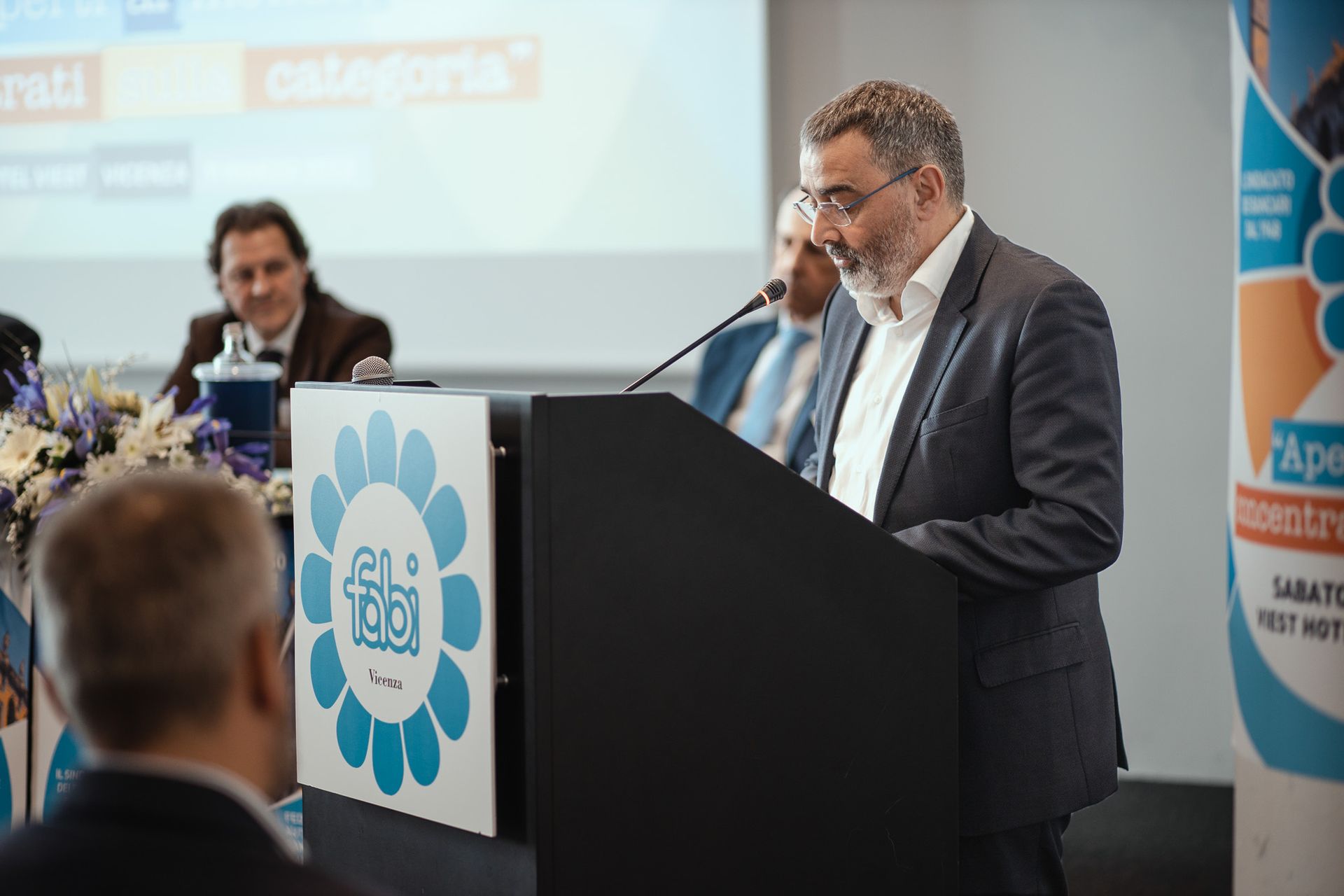 Un uomo in giacca e cravatta è in piedi su un podio e parla al microfono.