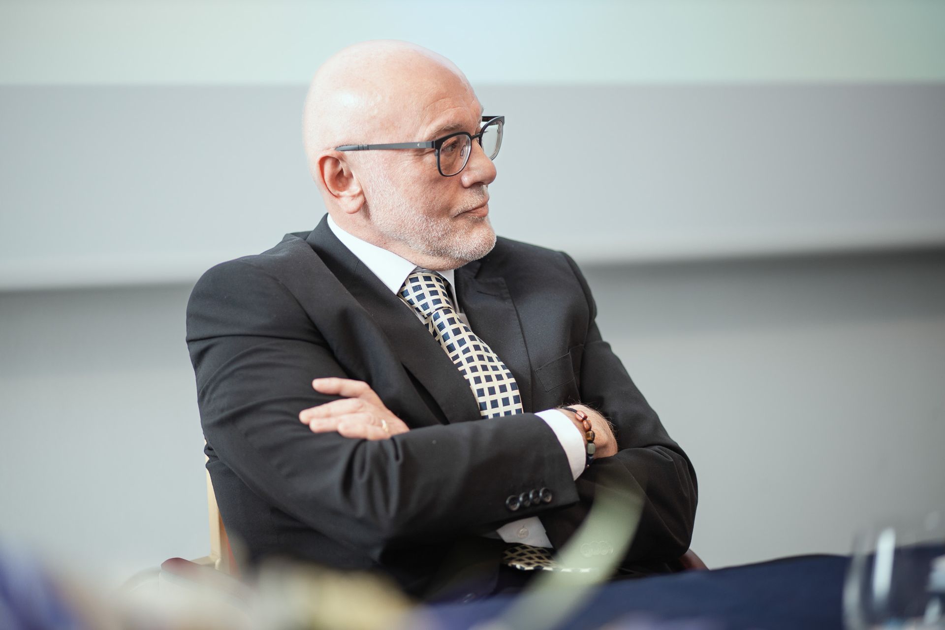 Un uomo in giacca e cravatta è seduto a un tavolo con le braccia incrociate.