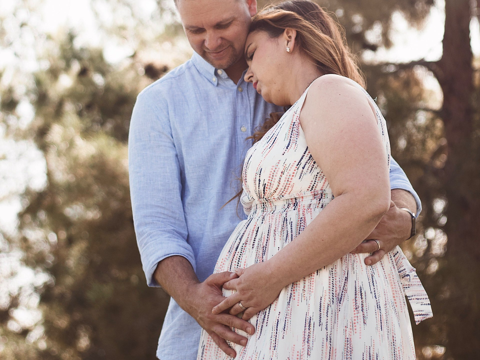 Un uomo abbraccia una donna incinta mentre lei le tiene la pancia.