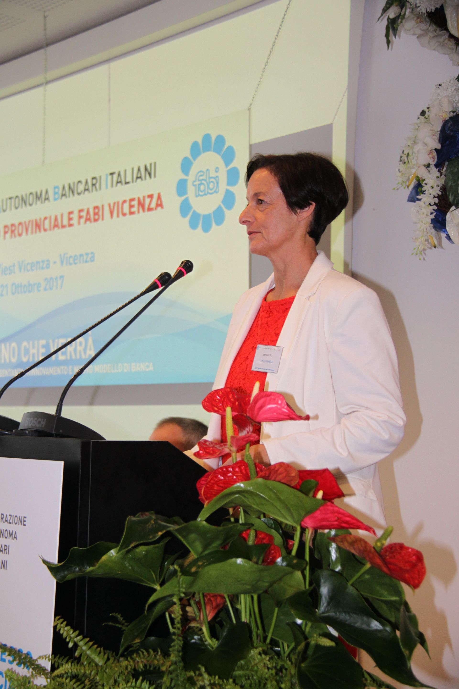Una donna sta su un podio con fiori davanti a uno schermo di proiezione
