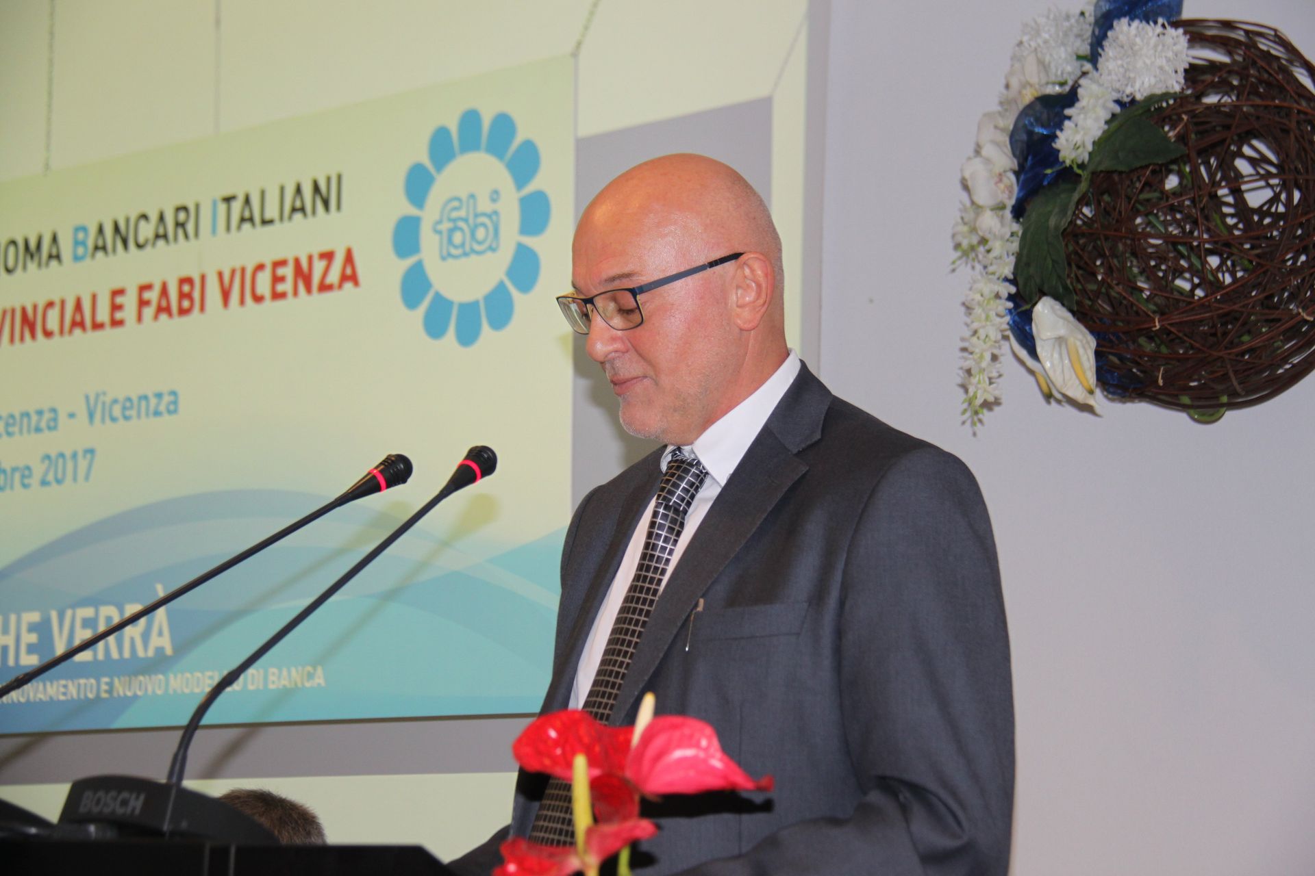 Un uomo in giacca e cravatta è in piedi davanti a due microfoni.