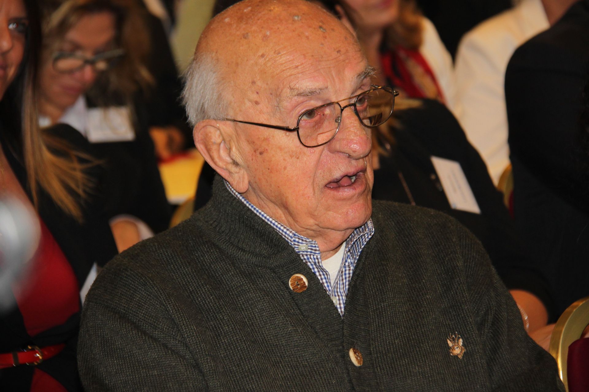 Un uomo anziano con gli occhiali è seduto in mezzo a una folla di persone