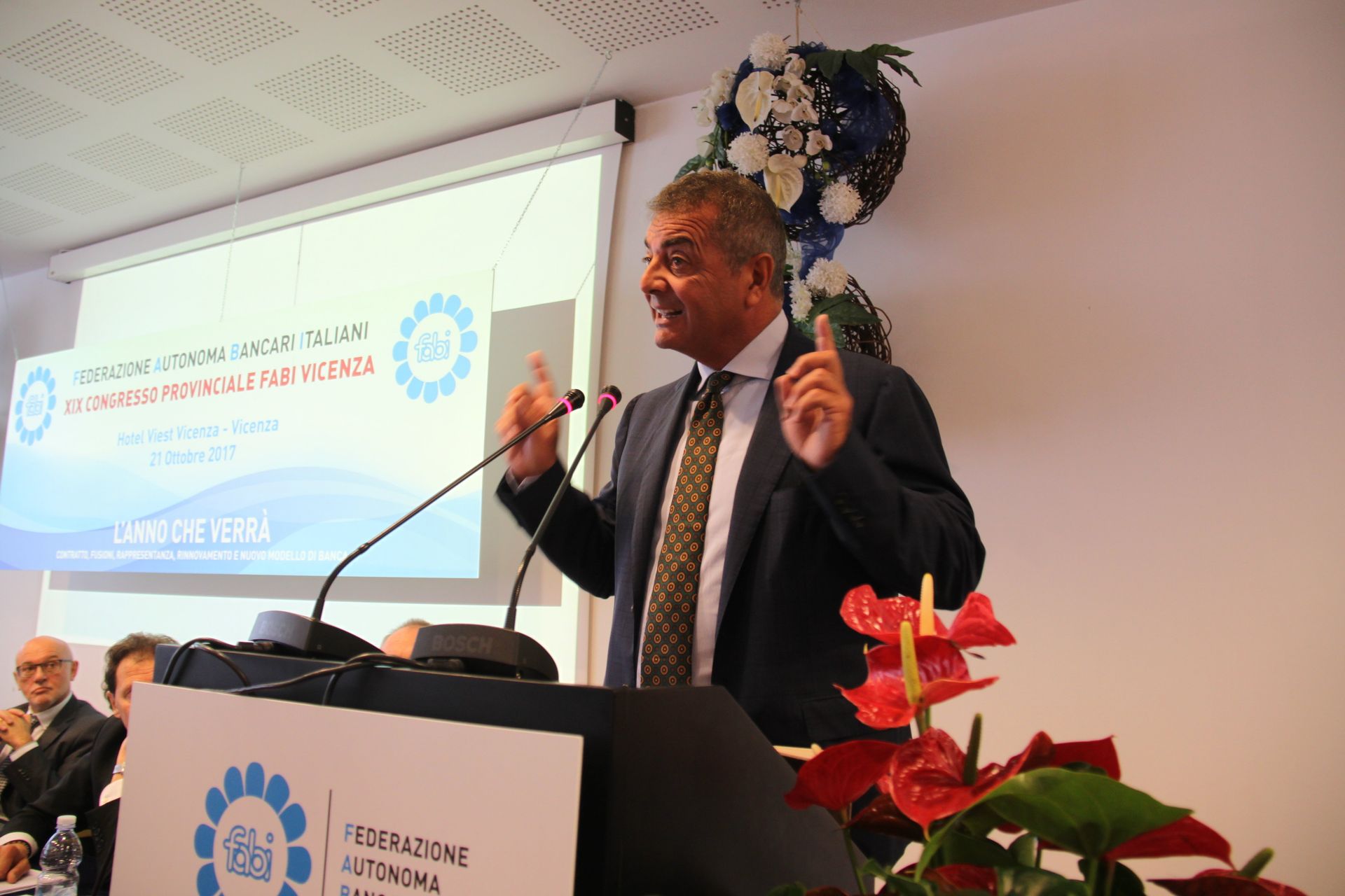 Un uomo in giacca e cravatta tiene un discorso su un podio.