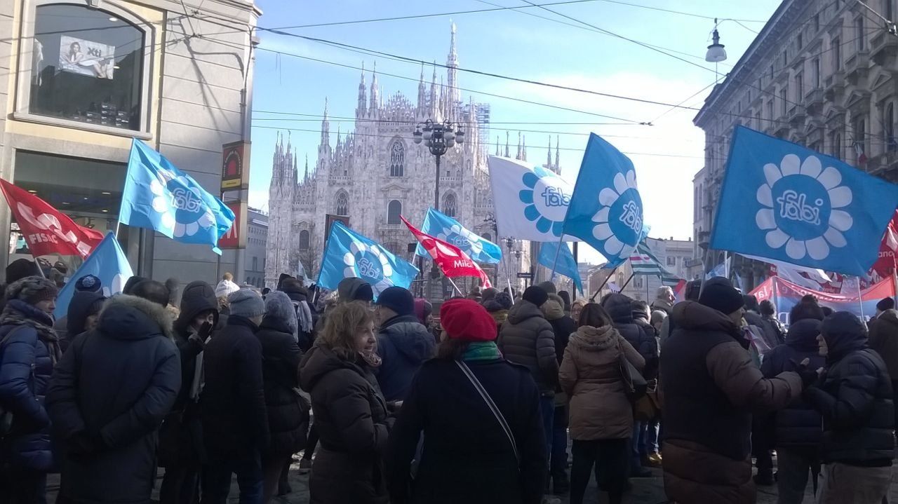 Un folto gruppo di persone tiene bandiere davanti a un edificio.
