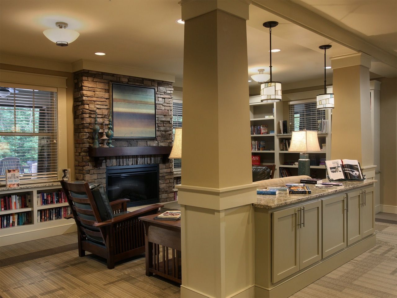 Indoor community lounge with a stone fireplace, bookshelves, and a granite-front counter.