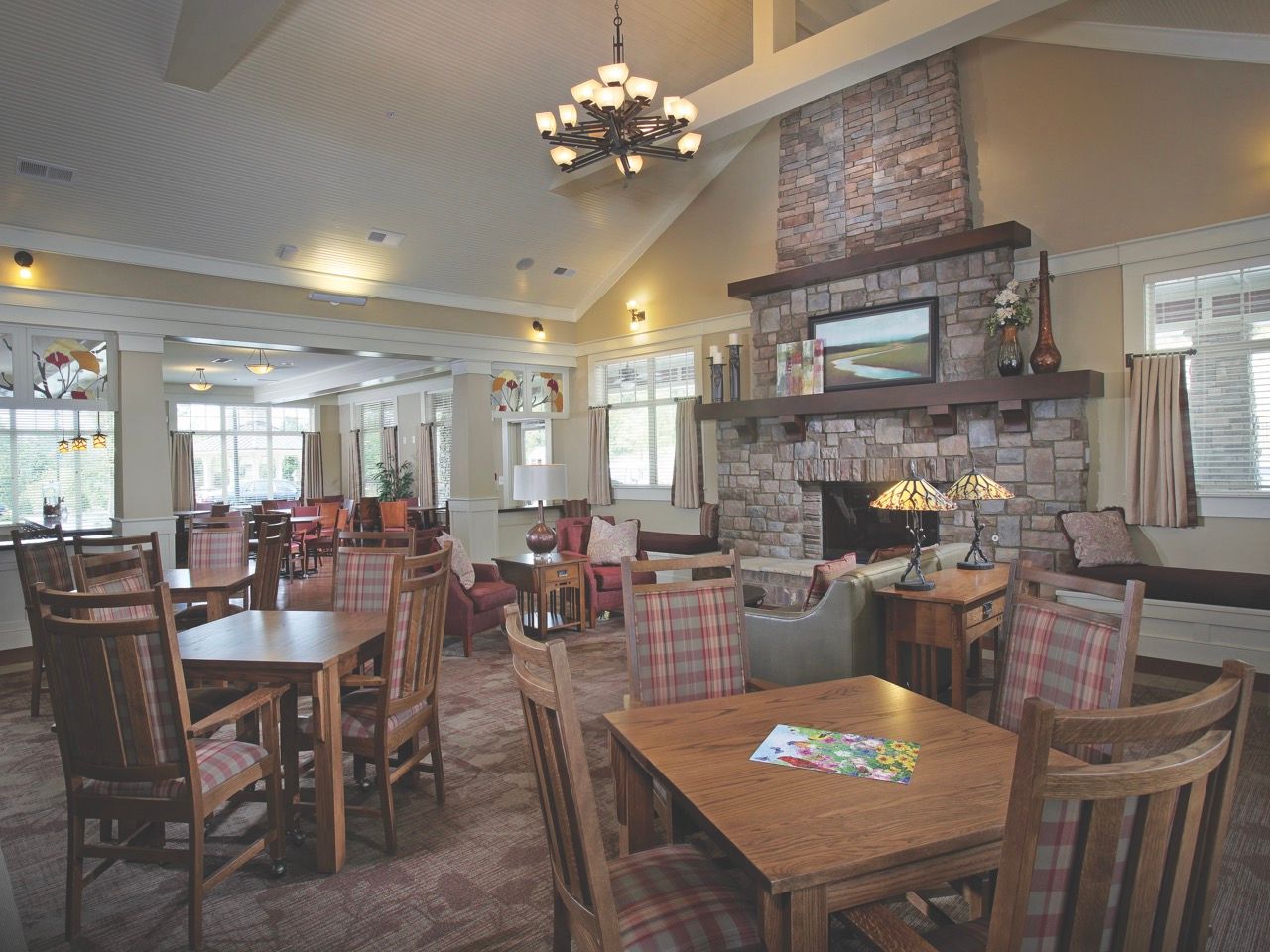 Spacious communal lounge with a stone fireplace, wooden tables, and cozy seating.