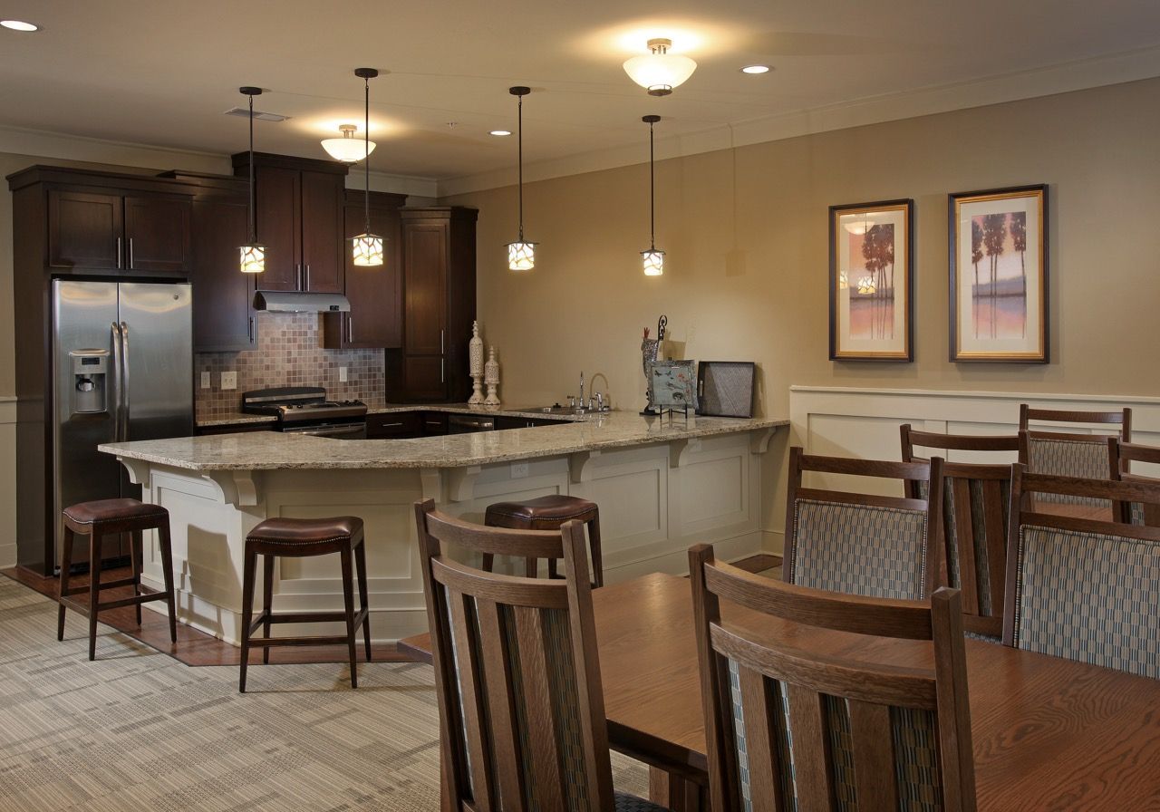 Community clubhouse kitchen with curved granite island, bar stools, pendant lights, and a dining area.