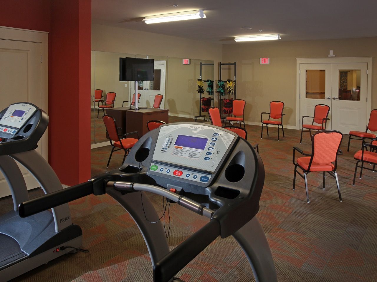 Fitness center with treadmill in the foreground and red chairs arranged around the room.