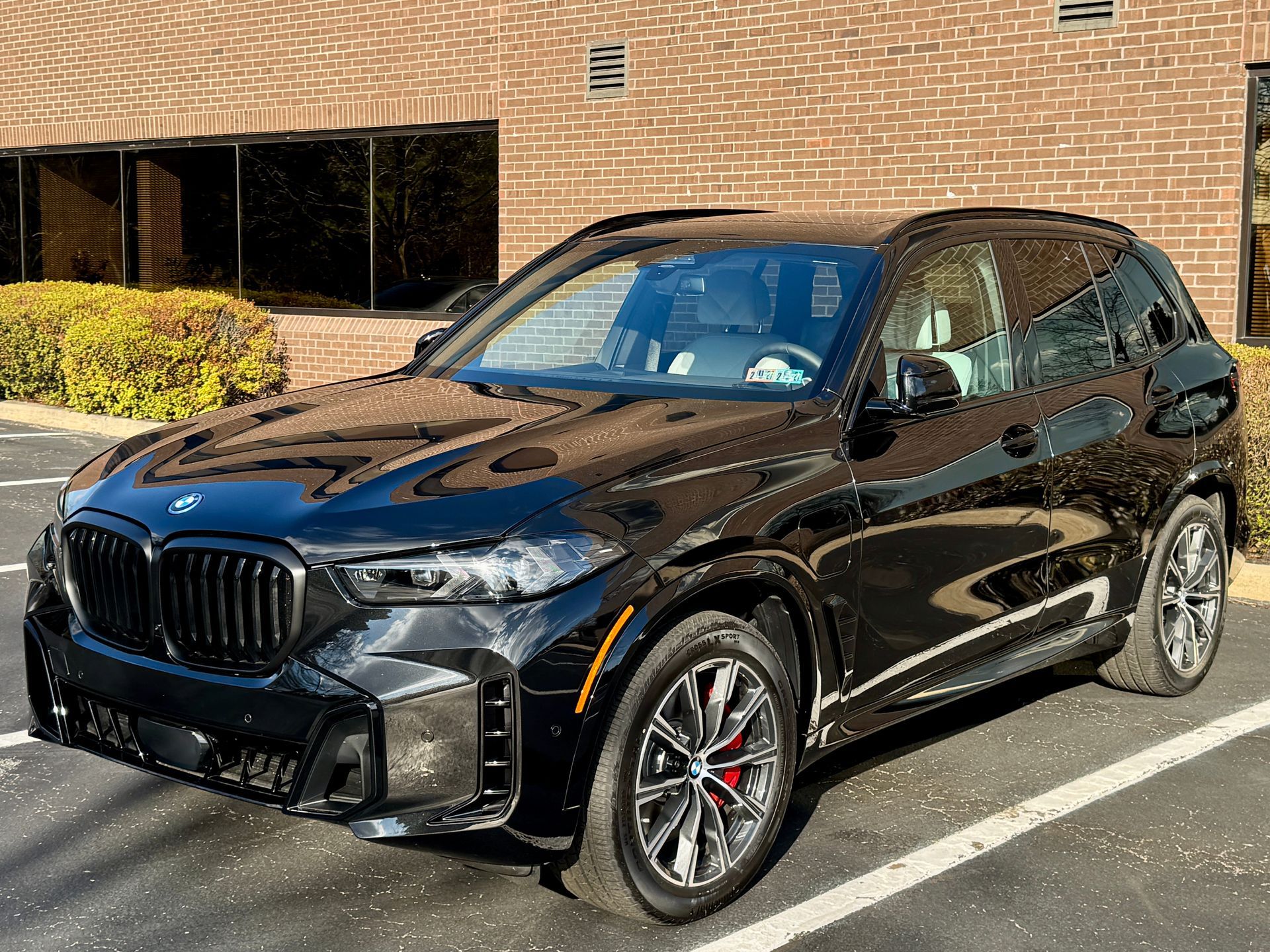 A black BMW X5 luxury SUV parked in a paved parking lot in front of a brick building.