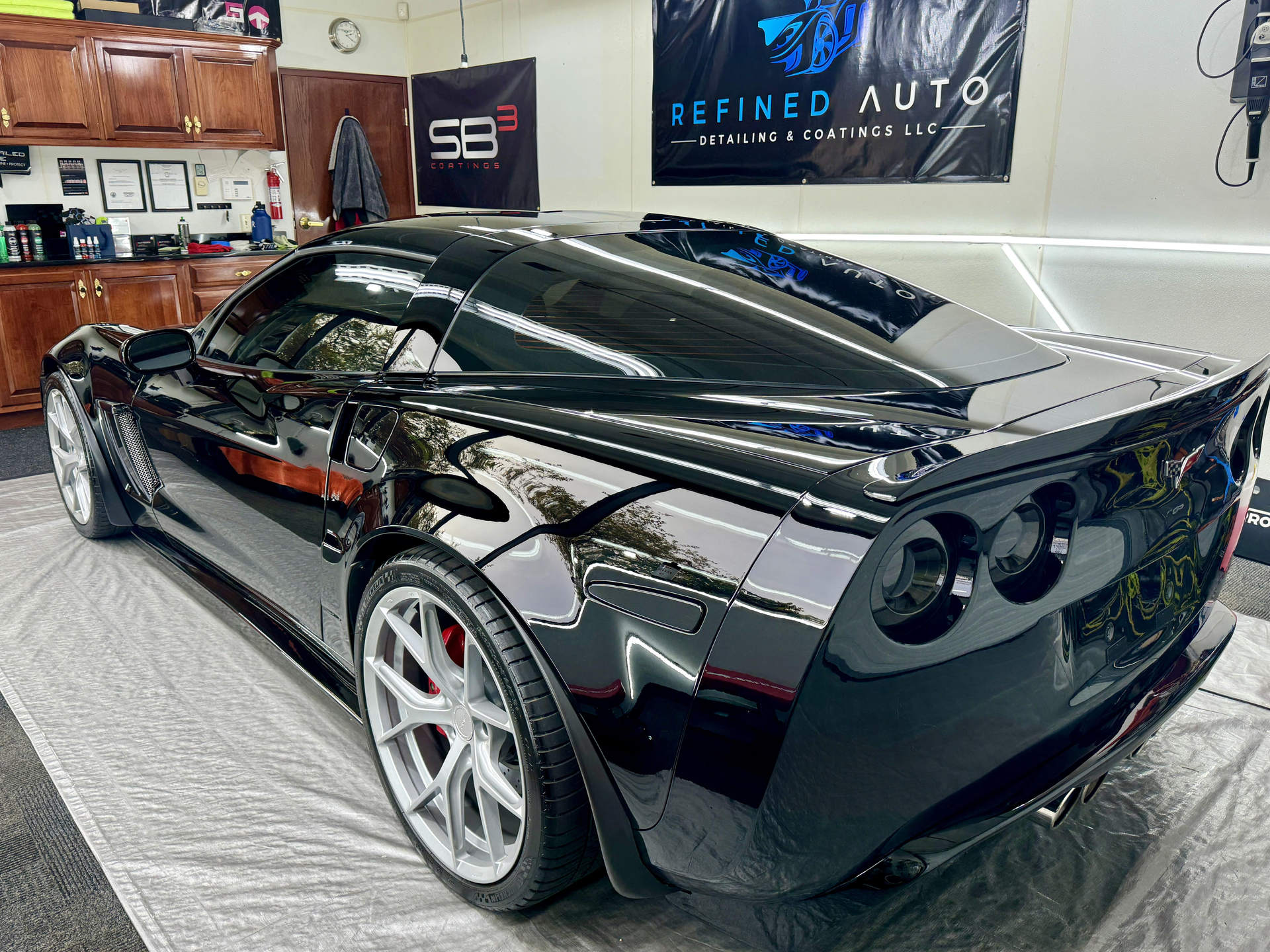 A black sports car is parked in a garage next to a sign that says refined auto.