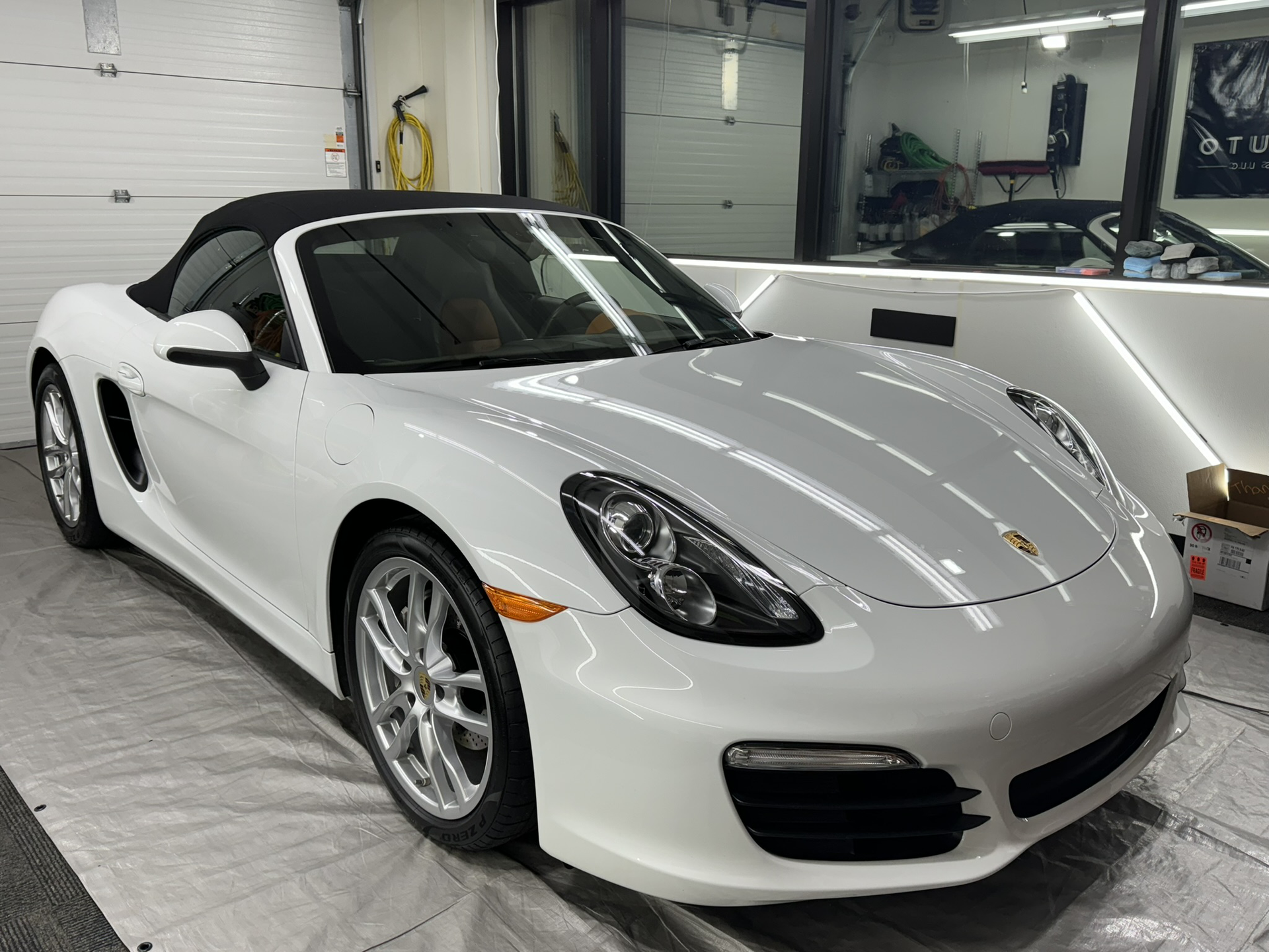 A white porsche boxster convertible is parked in a garage.