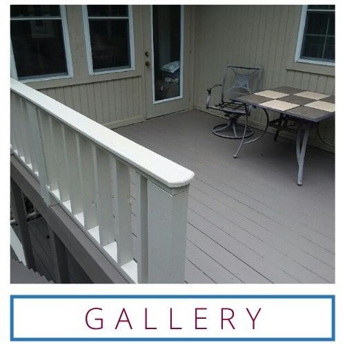 Patio deck with white railing, beige siding, and outdoor table and chair near a door