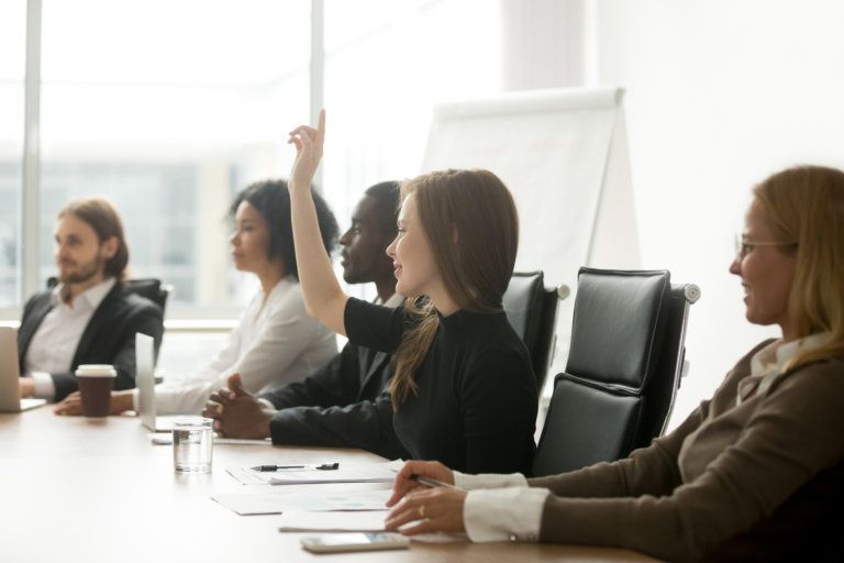 A group of people are sitting at a conference table with their hands up.