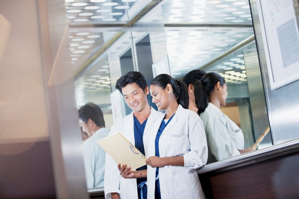 A man and a woman are standing next to each other in a hospital looking at a clipboard.