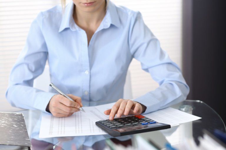 A woman is using a calculator and writing on a piece of paper