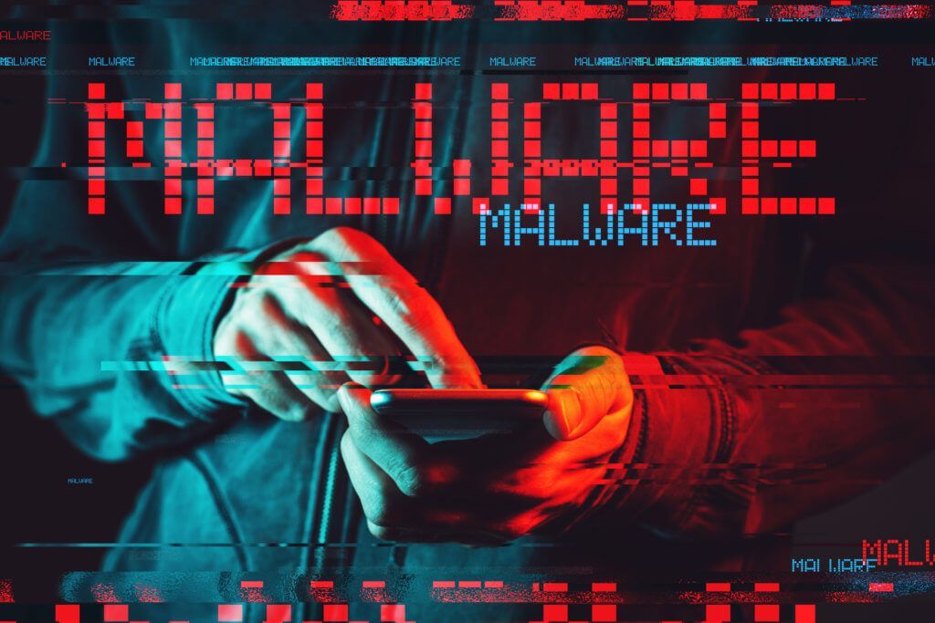 A person is holding a cell phone in front of a screen that says malware.