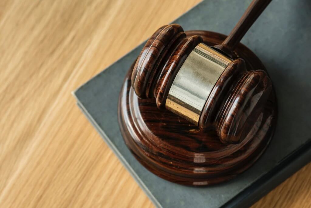 A wooden judge 's gavel is sitting on top of a book on a wooden table.