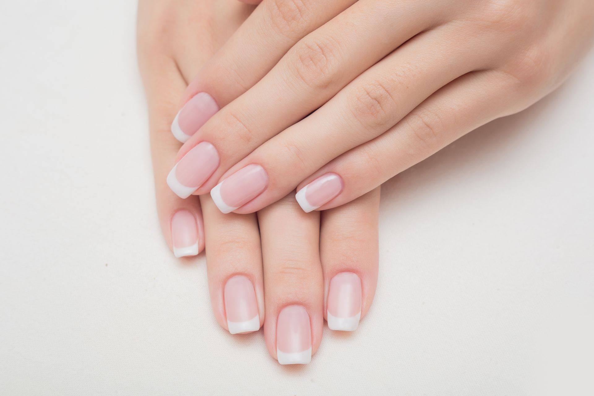 Eine Nahaufnahme der Hände einer Frau mit French-Maniküre auf weißem Hintergrund.
