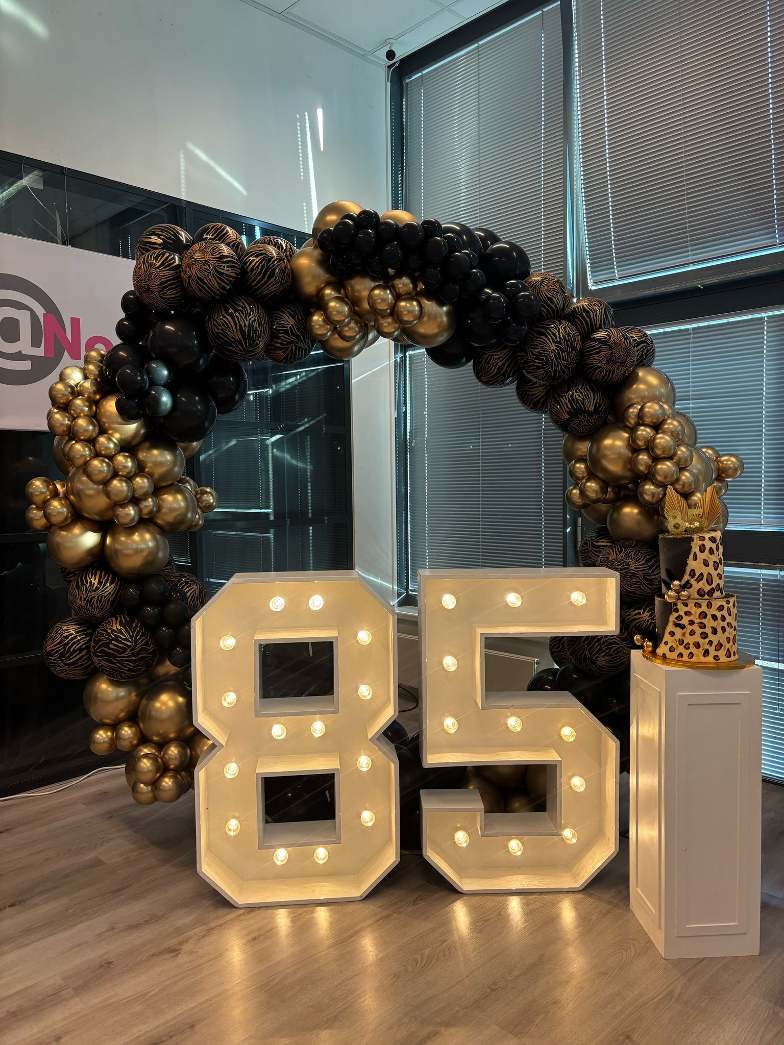 Een groot getal 85 is omgeven door ballonnen en lichtjes.