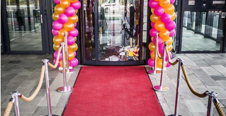 Een rode loper en ballonnen liggen opgesteld voor een gebouw.