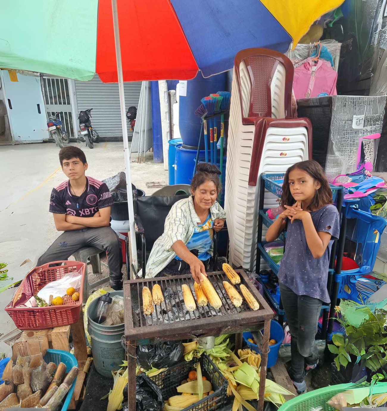 a group of people are sitting under an umbrella eating corn on the cob