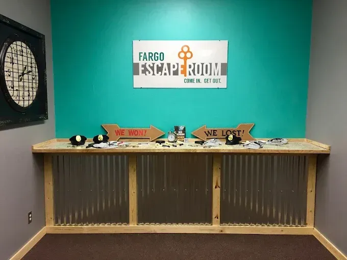 A teal-walled room with a Fargo Escape Room sign, a large clock, and a counter with 