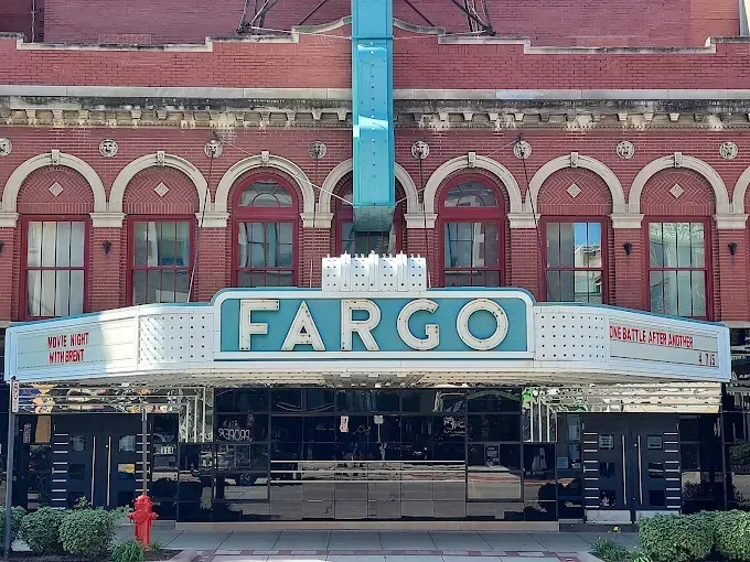 The historic Fargo Theatre features a red brick facade with arched windows and a large teal, illuminated marquee sign.