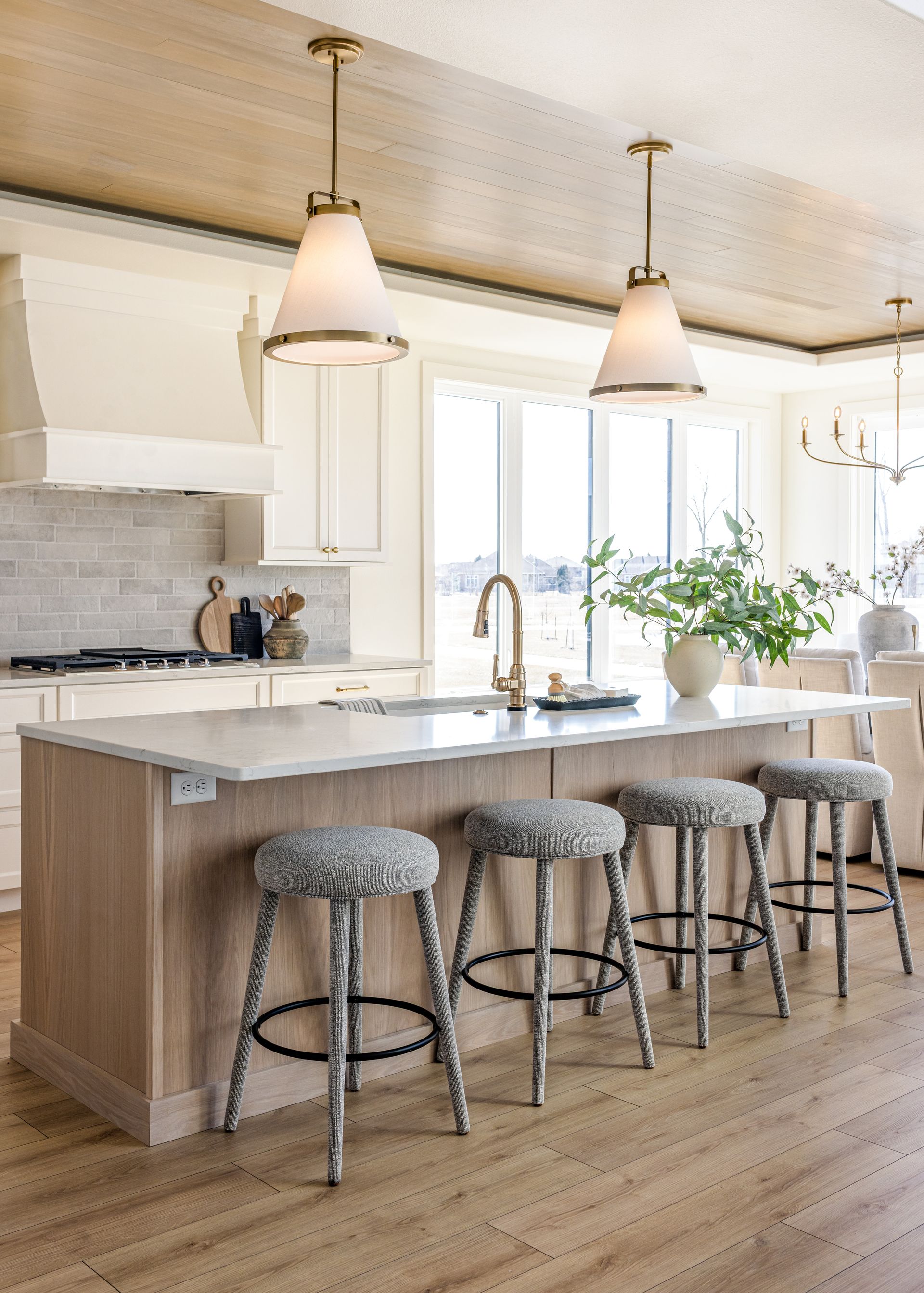 Modern kitchen with light wood island, marble countertop, pendant lights, and patterned stools.