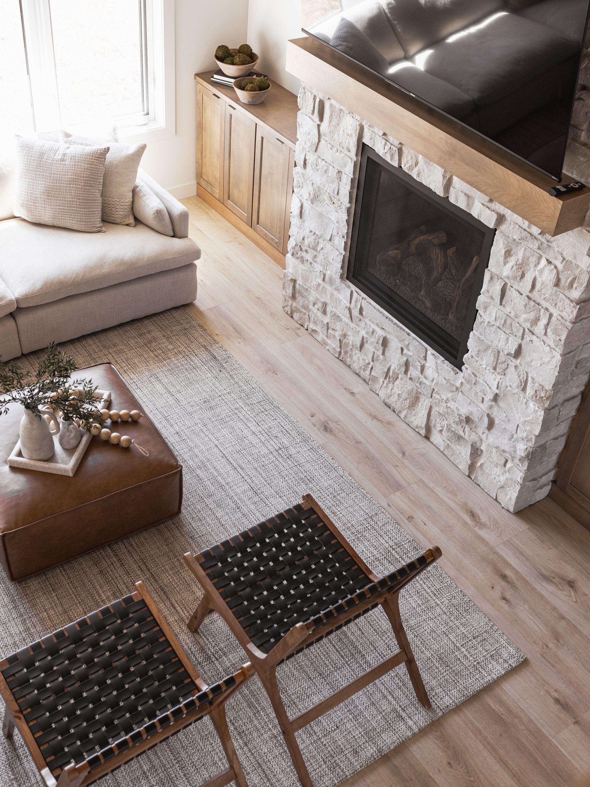 Living room with a stone fireplace, light wood cabinets, and leather chairs on a rug.