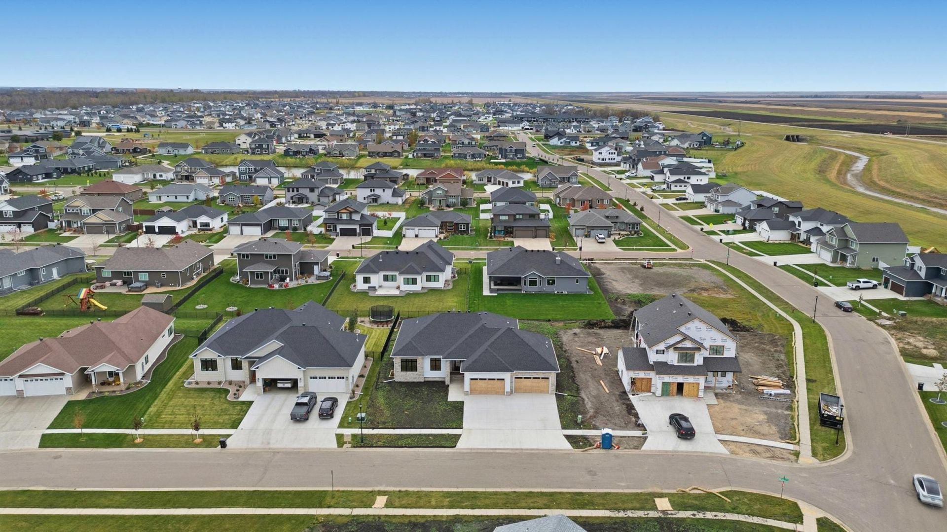 Aerial view of a suburban neighborhood with rows of houses, streets, and open fields in the distance