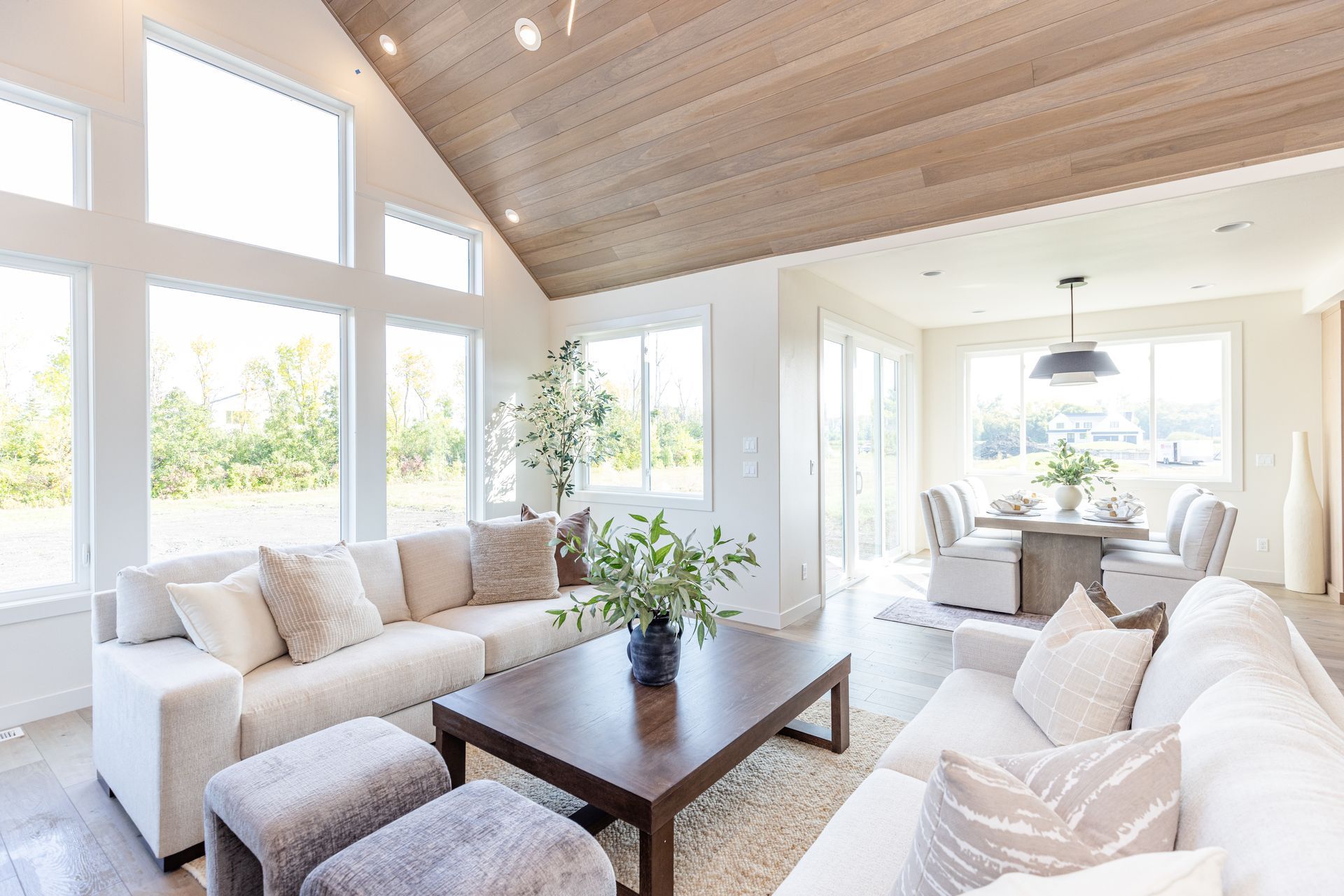 Bright living room with white sofas, wooden coffee table, large windows, and dining area.