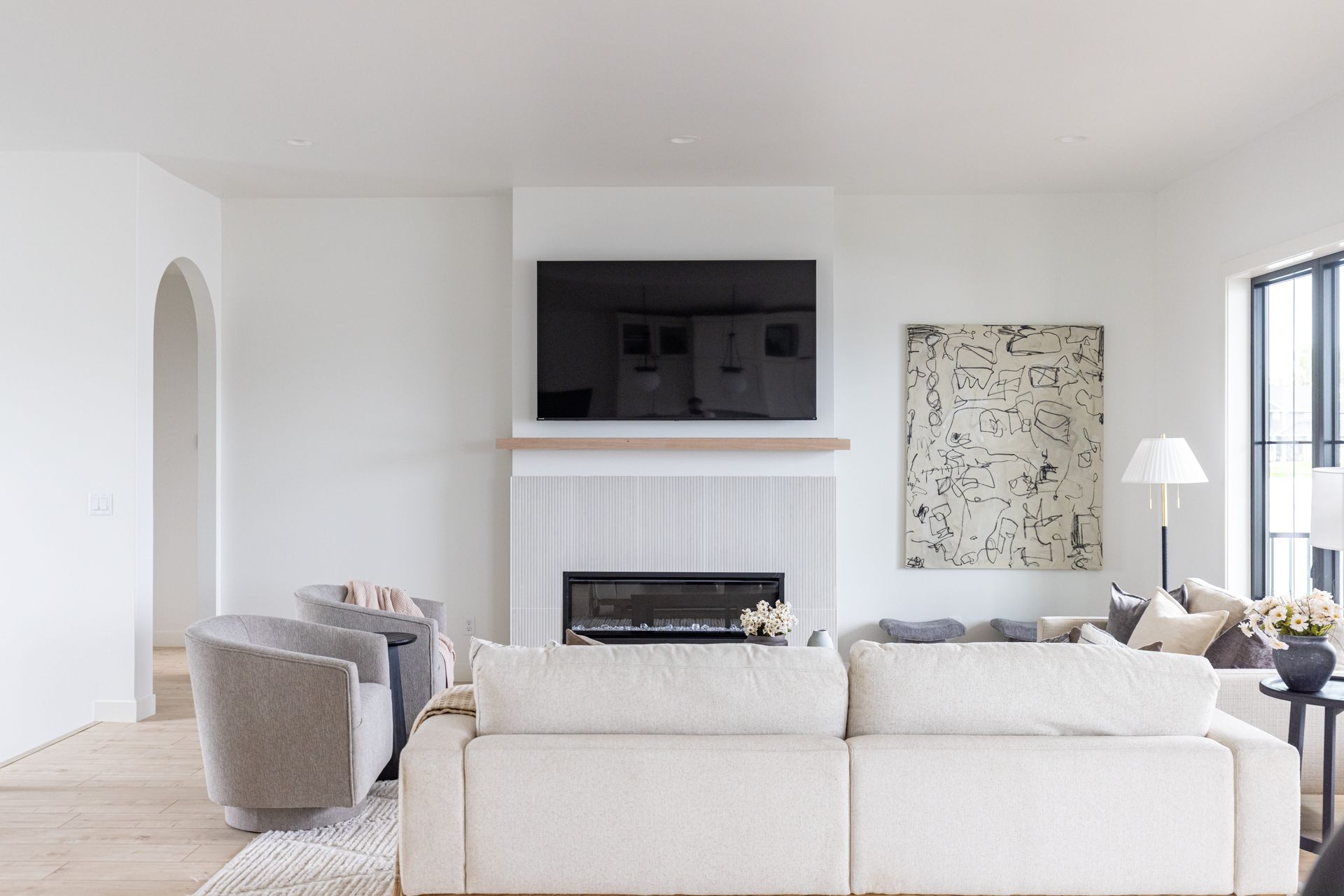 Living room with white walls, fireplace, sofa, chairs, artwork, and a TV.