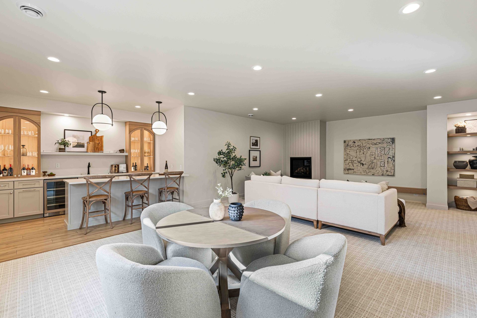 Spacious, modern basement with a bar, dining area, and seating. White walls, wood accents, and a light carpet.