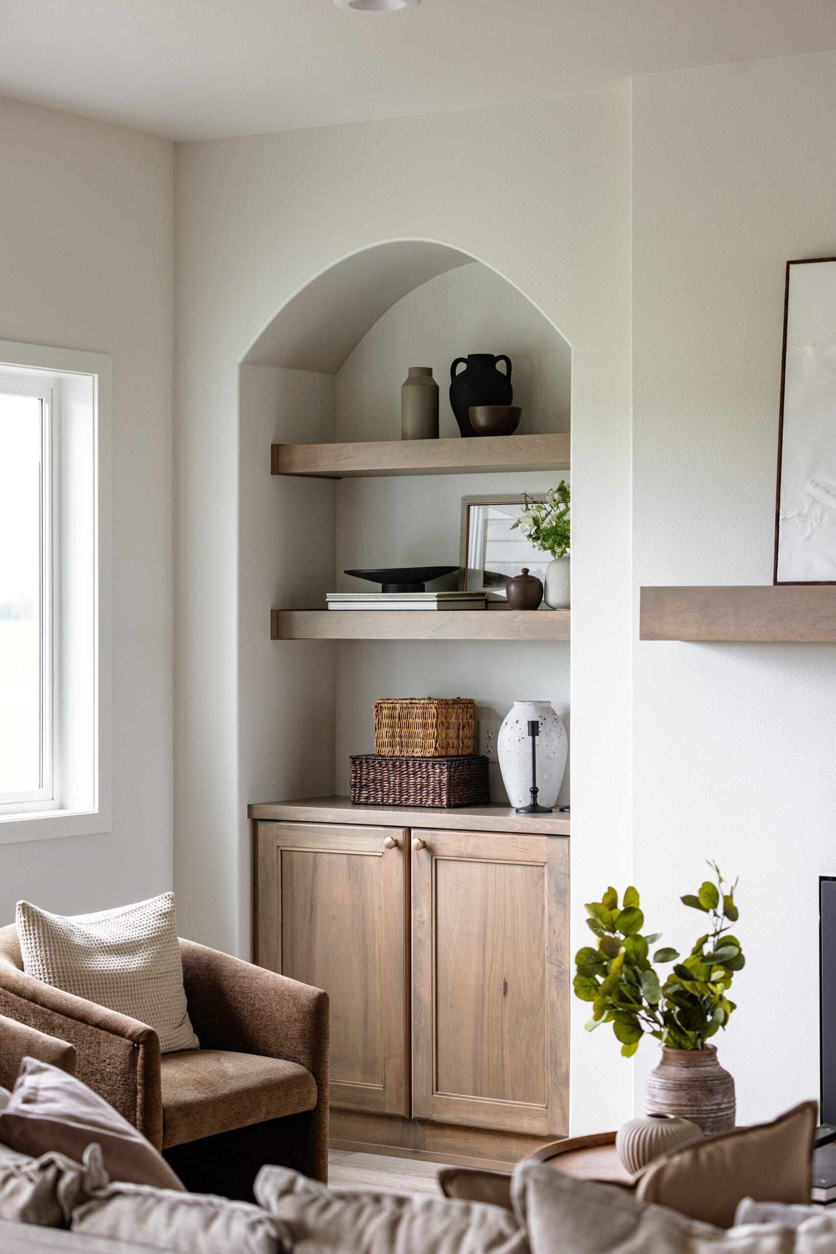 Built-in wooden shelves with decor inside a living room niche. Light wood cabinets below.