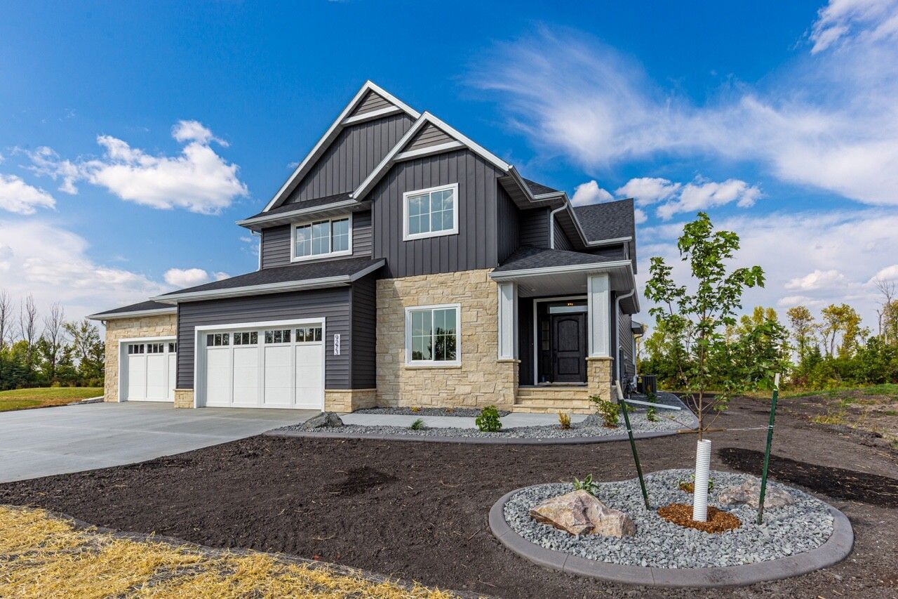 Modern two-story suburban house with charcoal vertical siding, stone masonry, a three-car garage, and a landscaped yard.