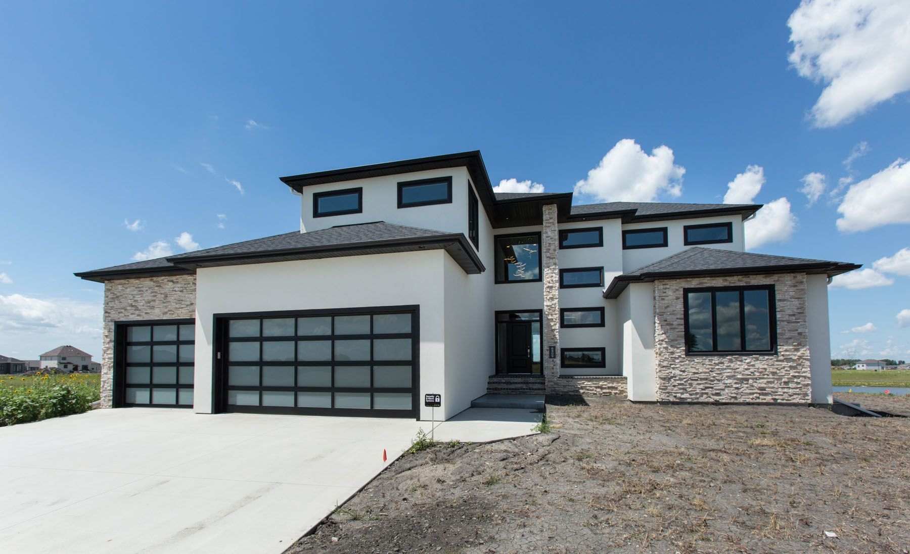 Modern two-story house with a white stucco exterior, black windows and garage doors, and stone accents against a blue sky.