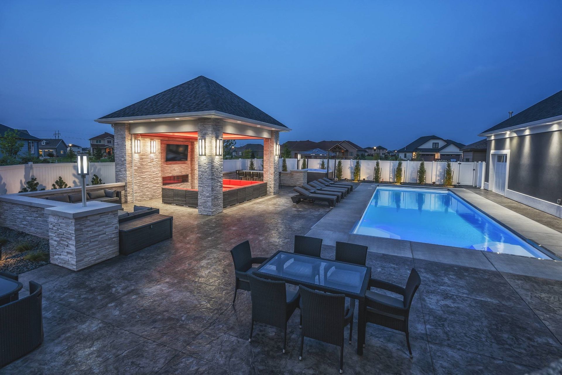 Luxury rooftop patio with a lit pool, dining table, and gazebo at dusk