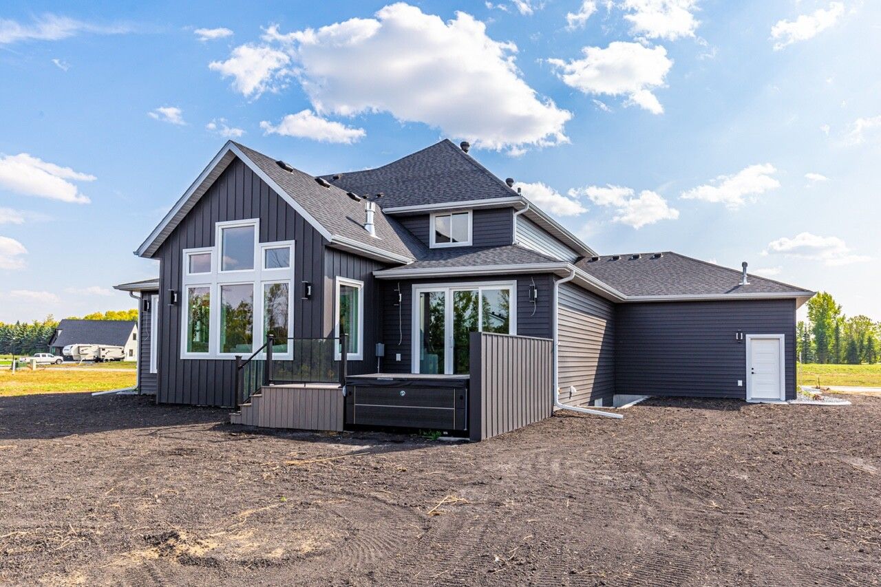 A dark-sided modern house with large windows and a small deck, set against a blue sky with clouds.