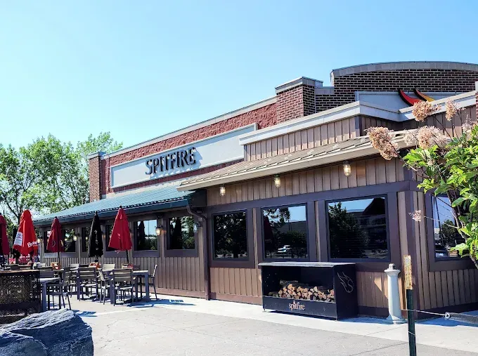 A Spitfire restaurant building with brown wooden siding, large windows, and outdoor patio tables under red umbrellas.