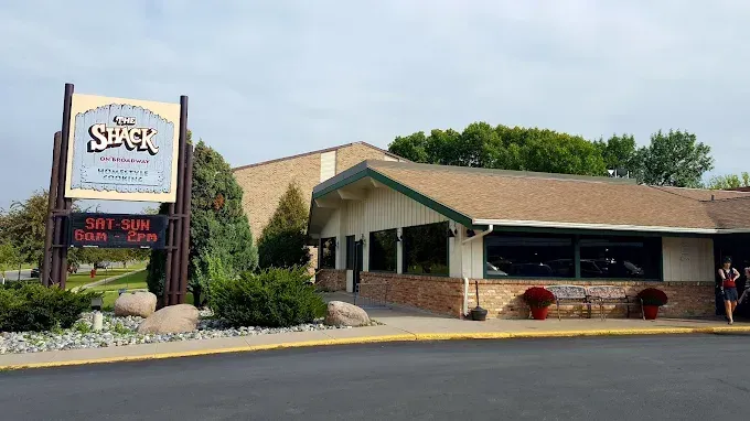 The Stack restaurant building under a cloudy sky with a large sign in the foreground and a person walking near the entry.