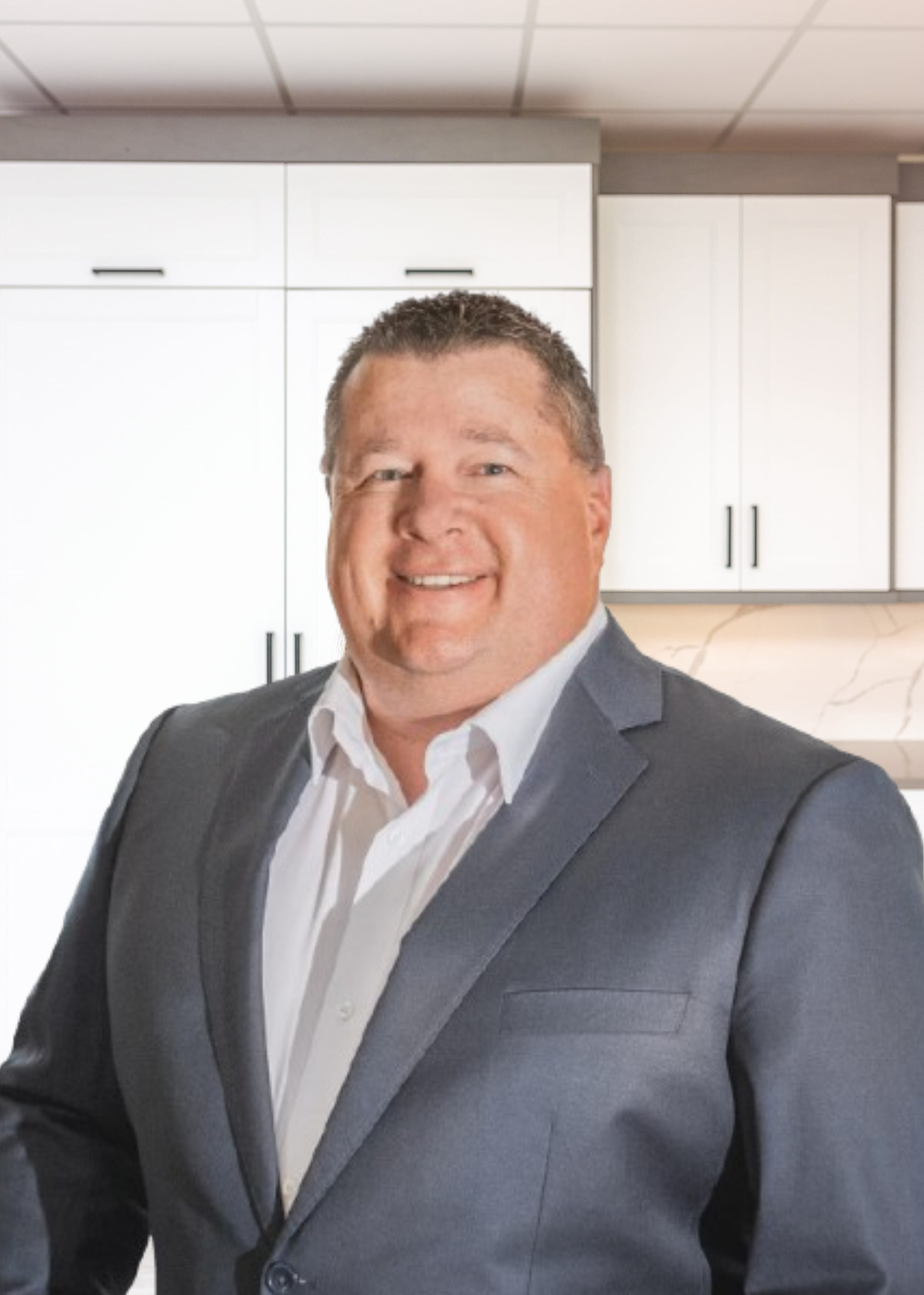 Man in a gray suit smiles in front of white cabinets.