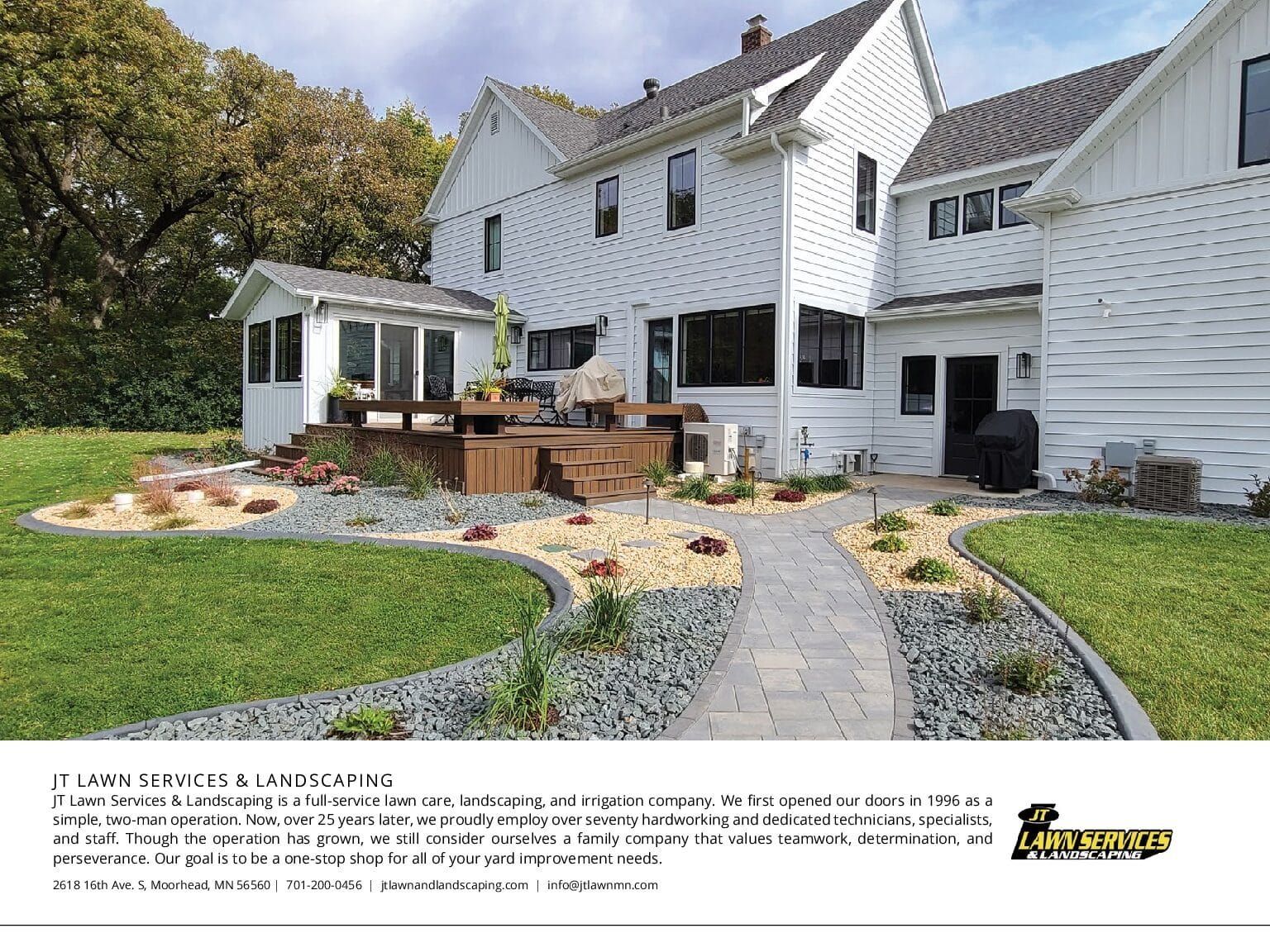 Backyard with white house, deck, and landscaped path with gravel and plants.
