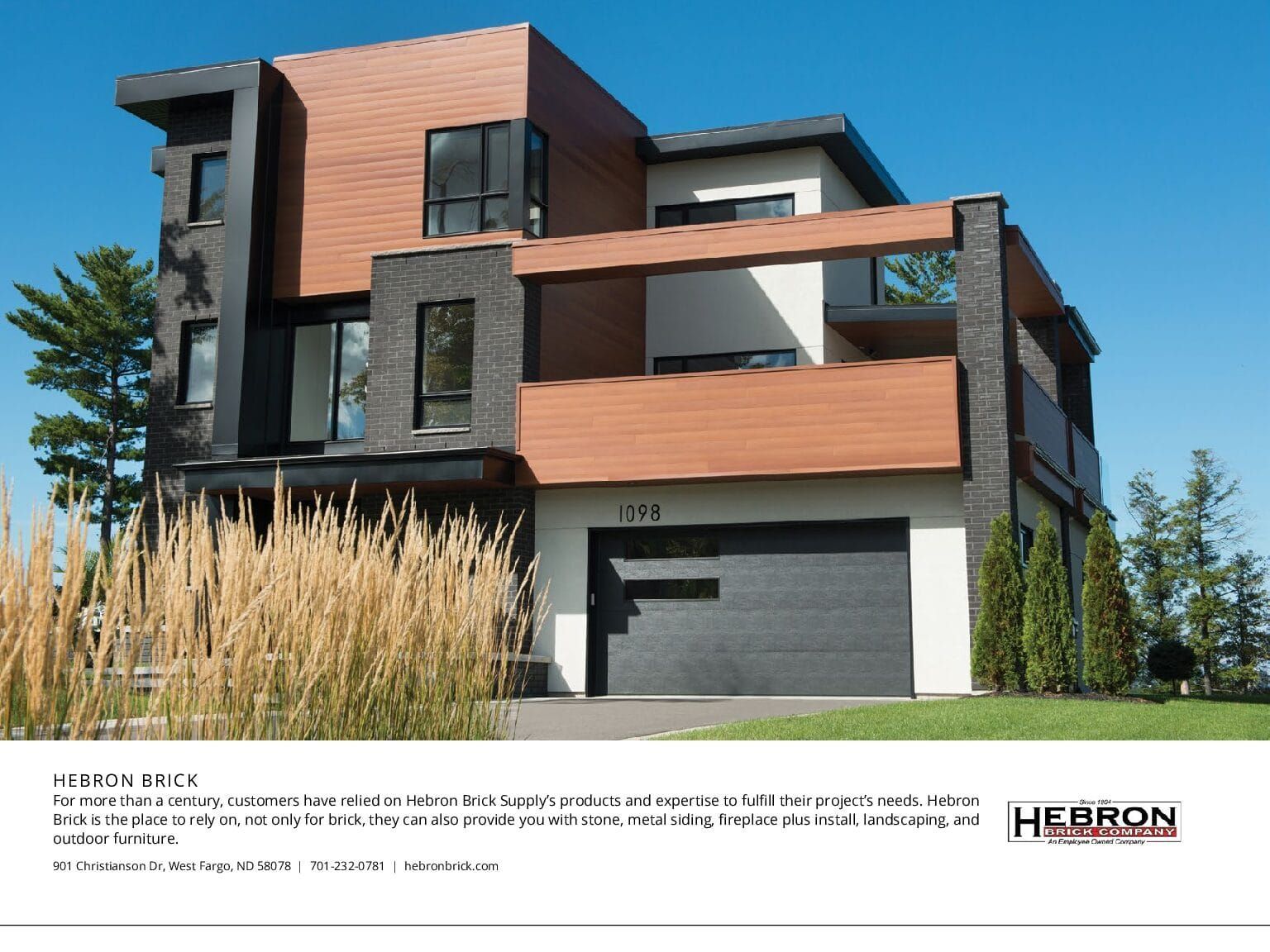 Modern two-story house with black and wood-tone exterior, attached garage, blue sky.
