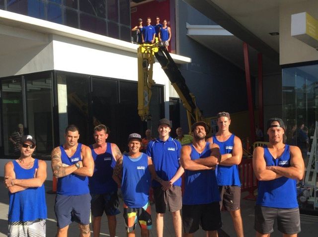 A group of men in blue tank tops are standing in front of a building