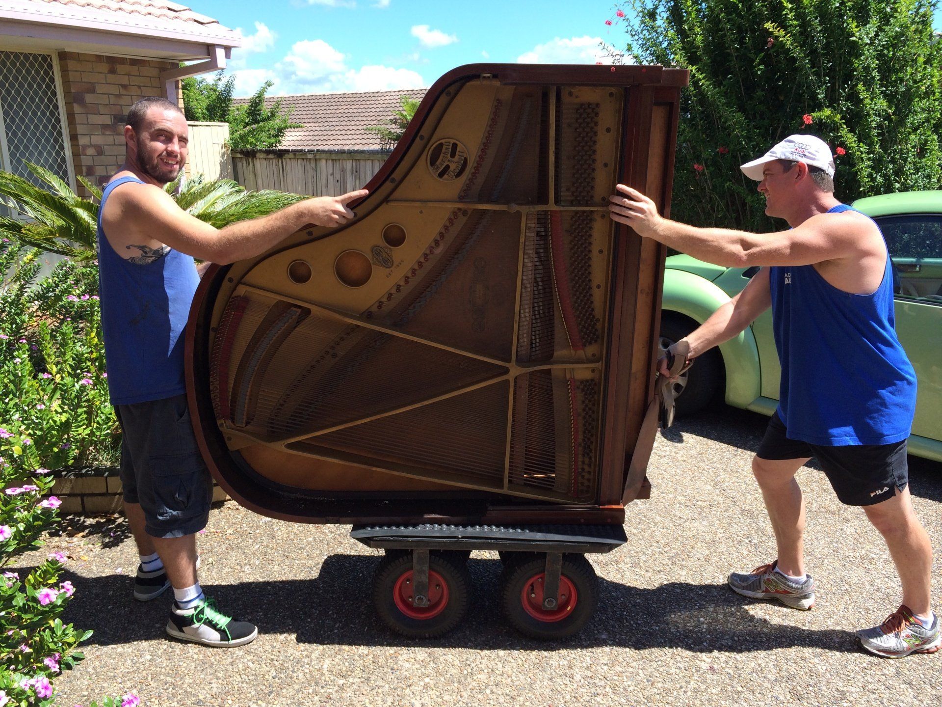 Two men are pushing a piano on a cart.